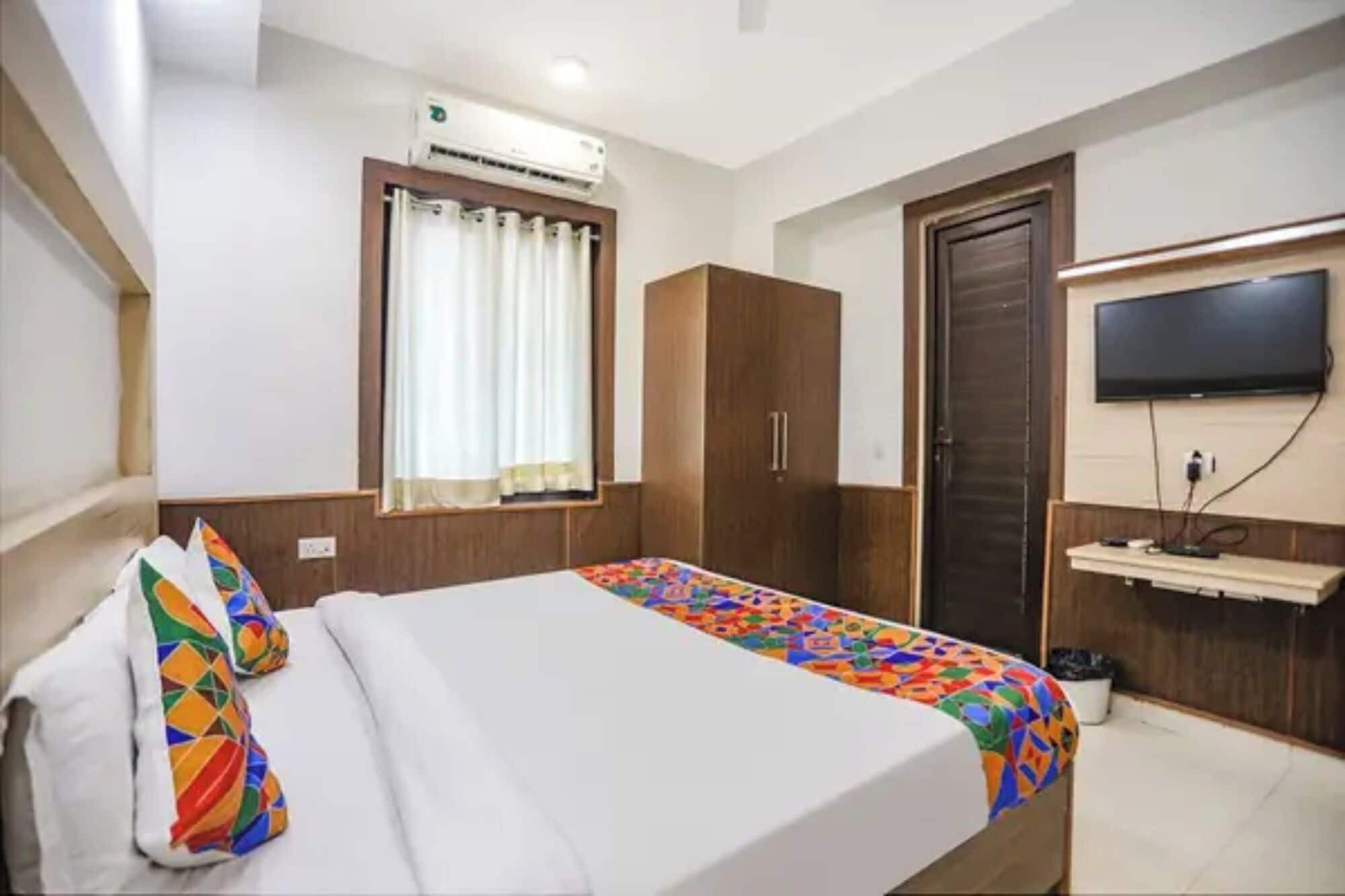 A hotel room with a bed, a wardrobe, a television, and an air conditioning unit.