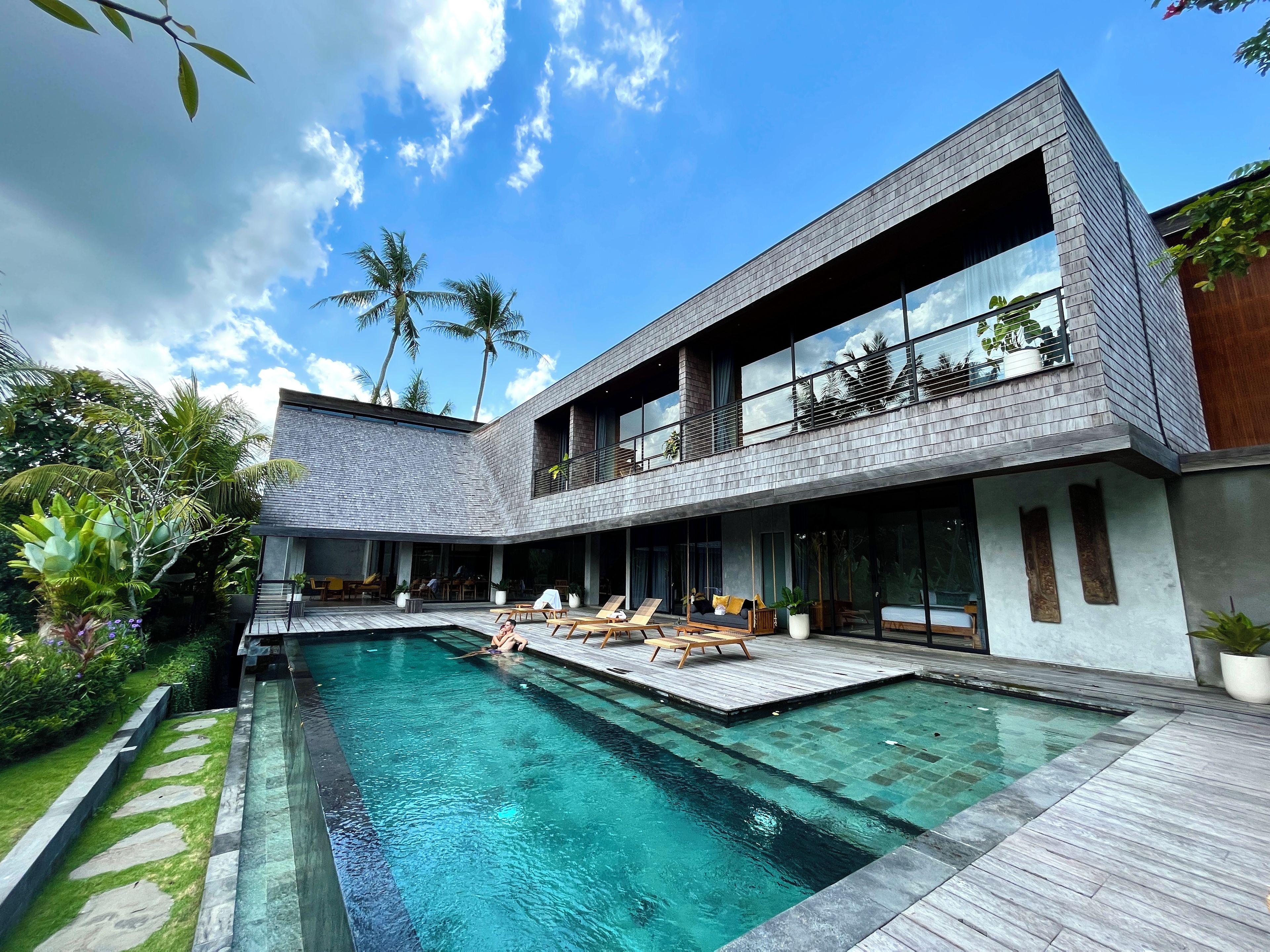 A modern two-story house with a swimming pool, outdoor seating, and lush greenery.