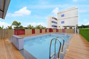A swimming pool with a wooden deck, surrounded by a low wall with patterned tiles and red decorative panels. - Deluxe Room Sonia Mahi Inn (Nagercoil)