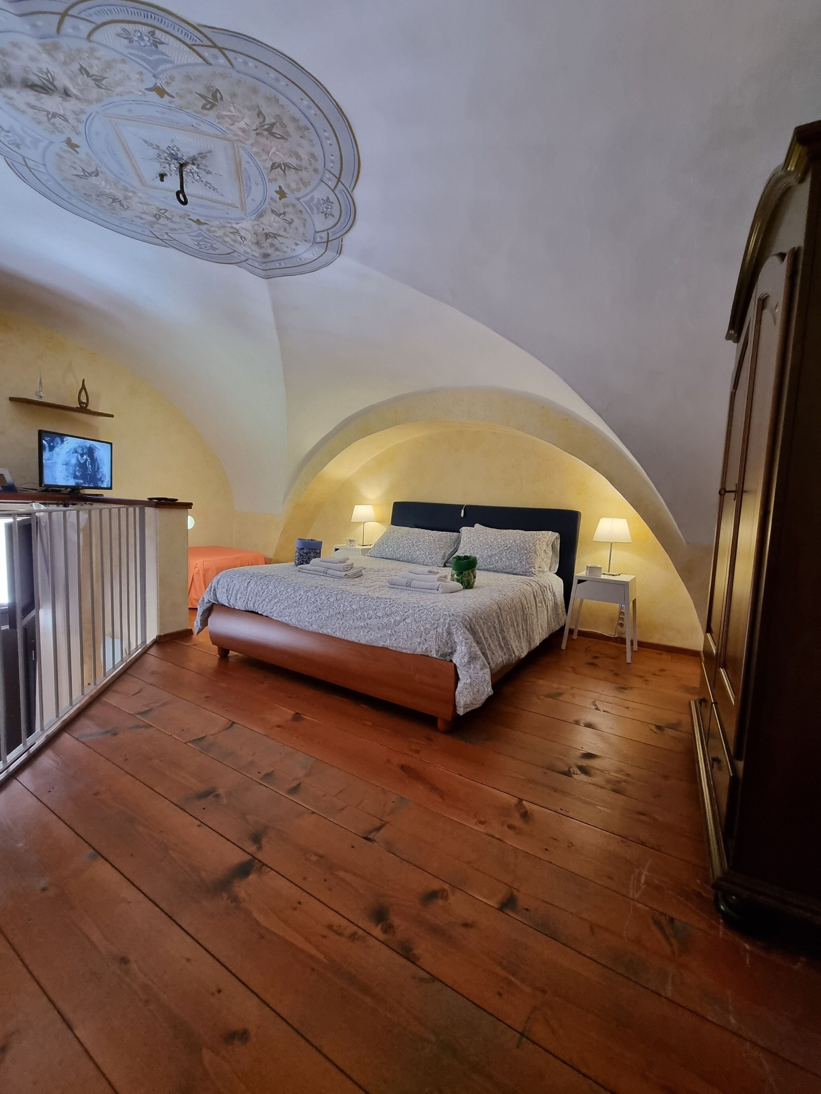 A bedroom with a sloped ceiling, a bed with a headboard, a bedside table with a lamp, and a television on a stand.