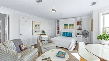 A modern bedroom with a bed, two armchairs, a white coffee table, and a bedside table with a lamp.