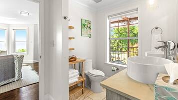 A bathroom with a large sink, toilet, and window. There is a towel rack and a painting on the wall.