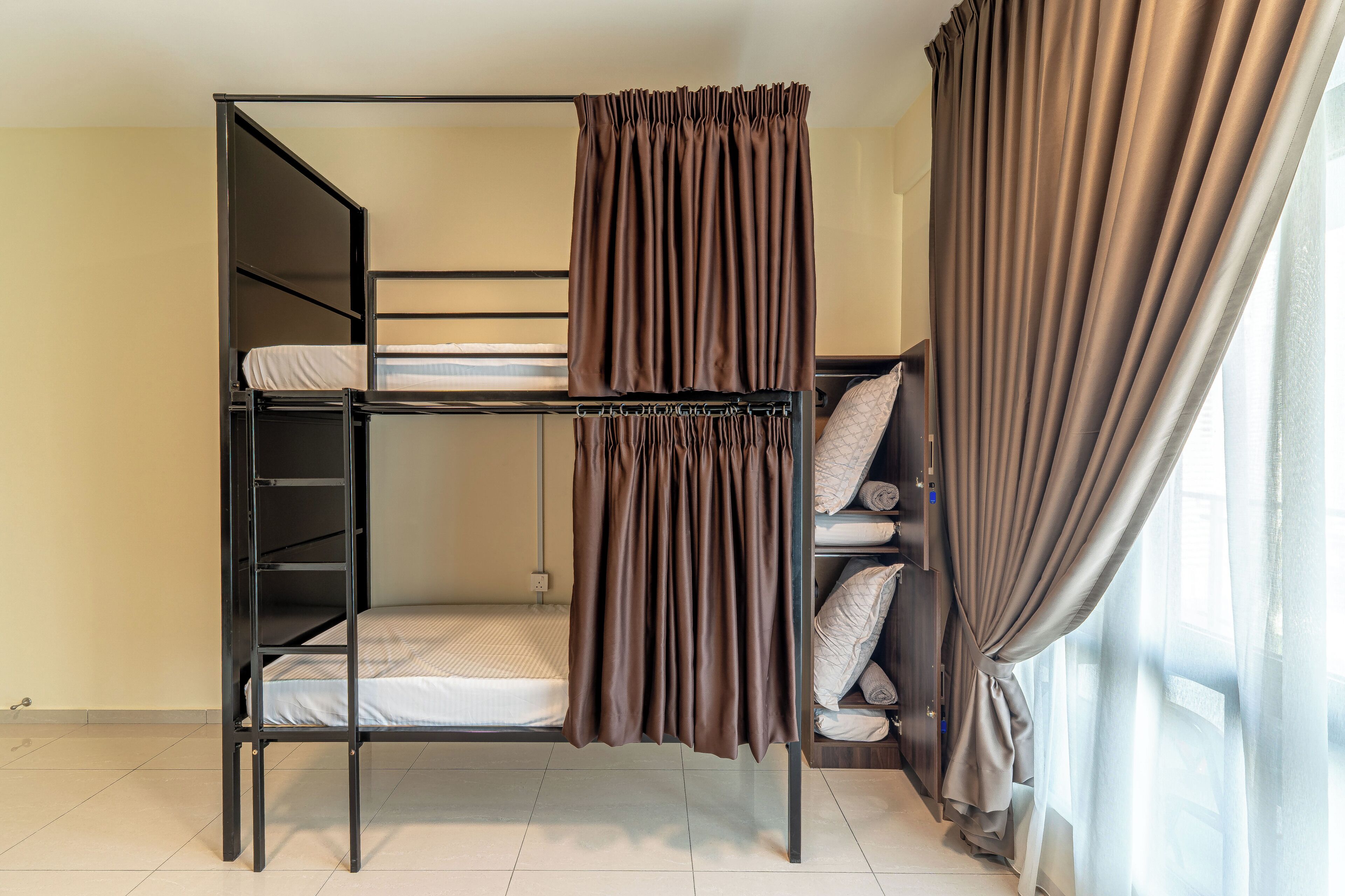 A bunk bed with a curtain divider, a shelf with pillows, and a window with curtains.