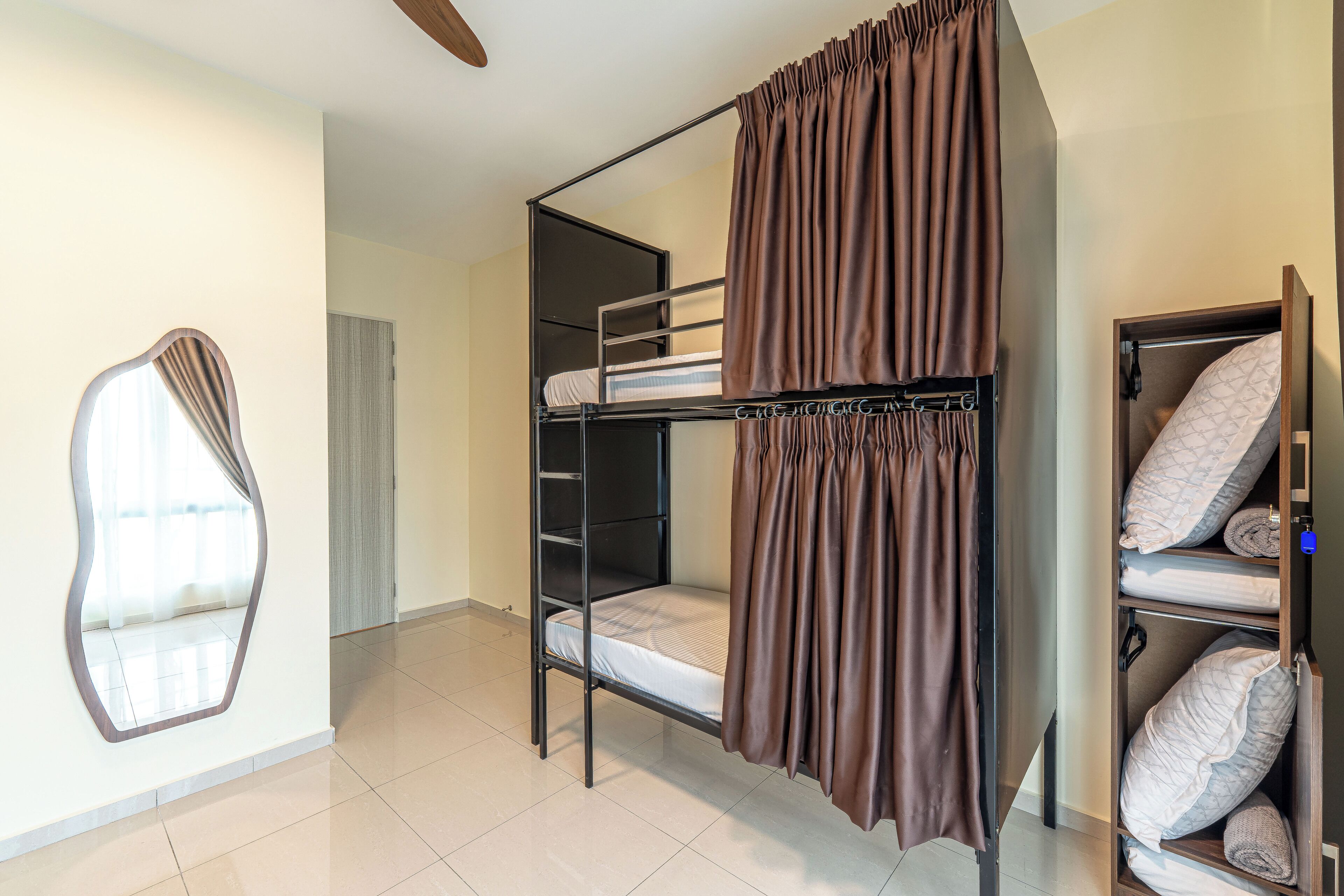 Habitación con literas, cortina, espejo y unidad de almacenamiento con almohadas.