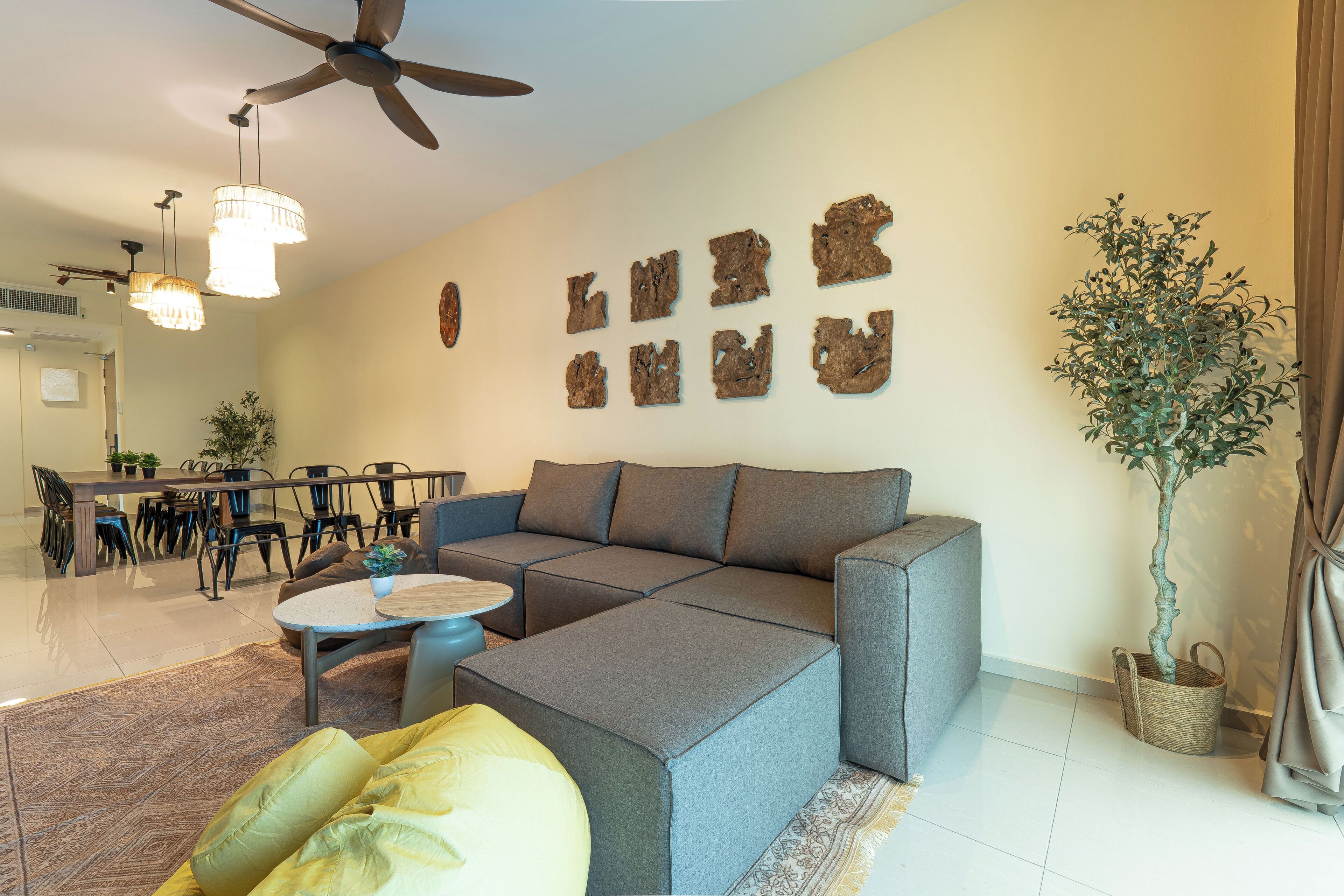 A modern living room with a sectional sofa, a dining area with chairs, a ceiling fan, and wall-mounted decor.