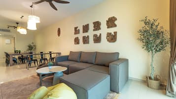 A modern living room with a sectional sofa, a dining area with chairs, a ceiling fan, and wall-mounted decor.