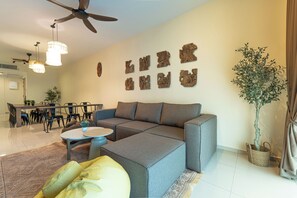 A modern living room with a sectional sofa, a dining area with chairs, a ceiling fan, and wall-mounted decor. - Legasi Kampung Baru BackpackerGuesthouse (Kuala Lumpur)