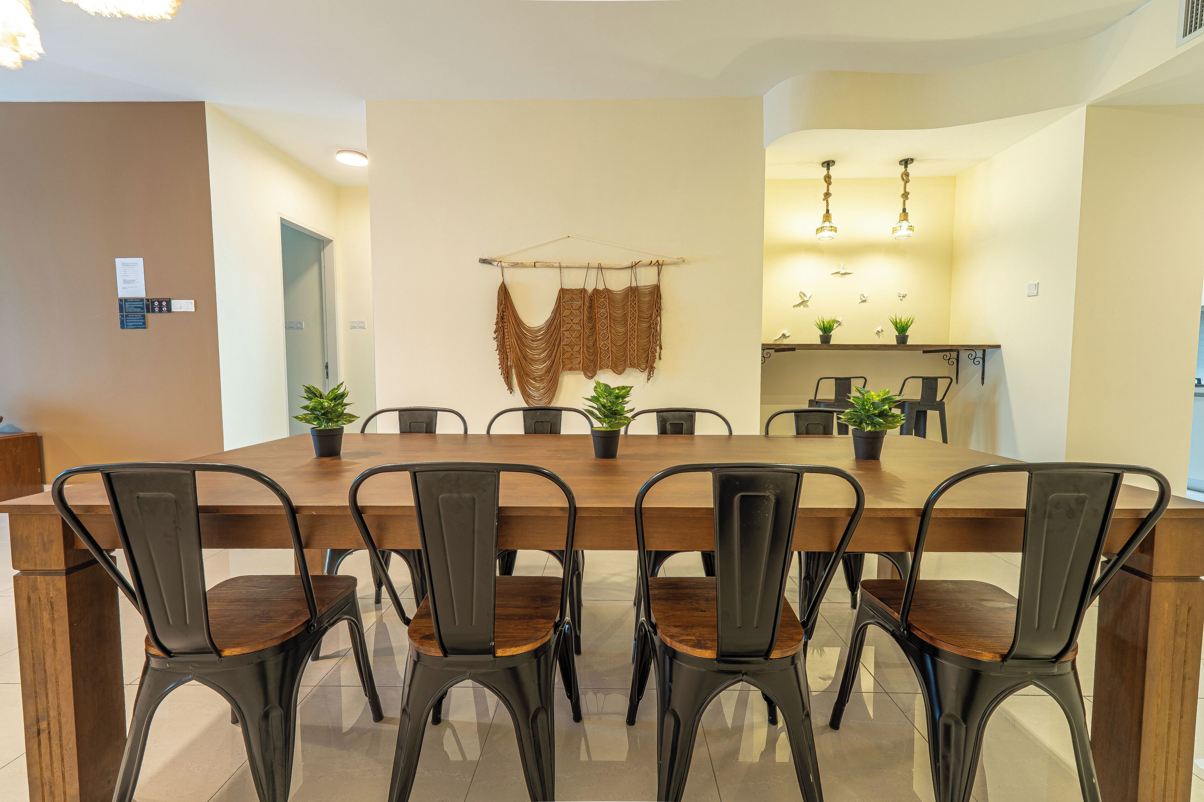 A dining area with a long wooden table, six chairs, and potted plants.