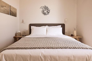 Un lit bien fait, avec une couverture à motifs, une tête de lit et deux tables de chevet, dont l’une est ornée d’une lampe et d’un vase.