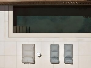 Ein moderner Außenbereich mit Pool, zwei Liegestühlen und einem kleinen Tisch.