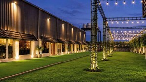 Un edificio con una estructura larga y estrecha, un área verde al frente y luces colgantes.