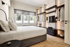 A modern bedroom with a bed, a TV, a wardrobe, and a window with blinds. - Estia Athens – Your Luxurious Urban Retreat (Athens)
