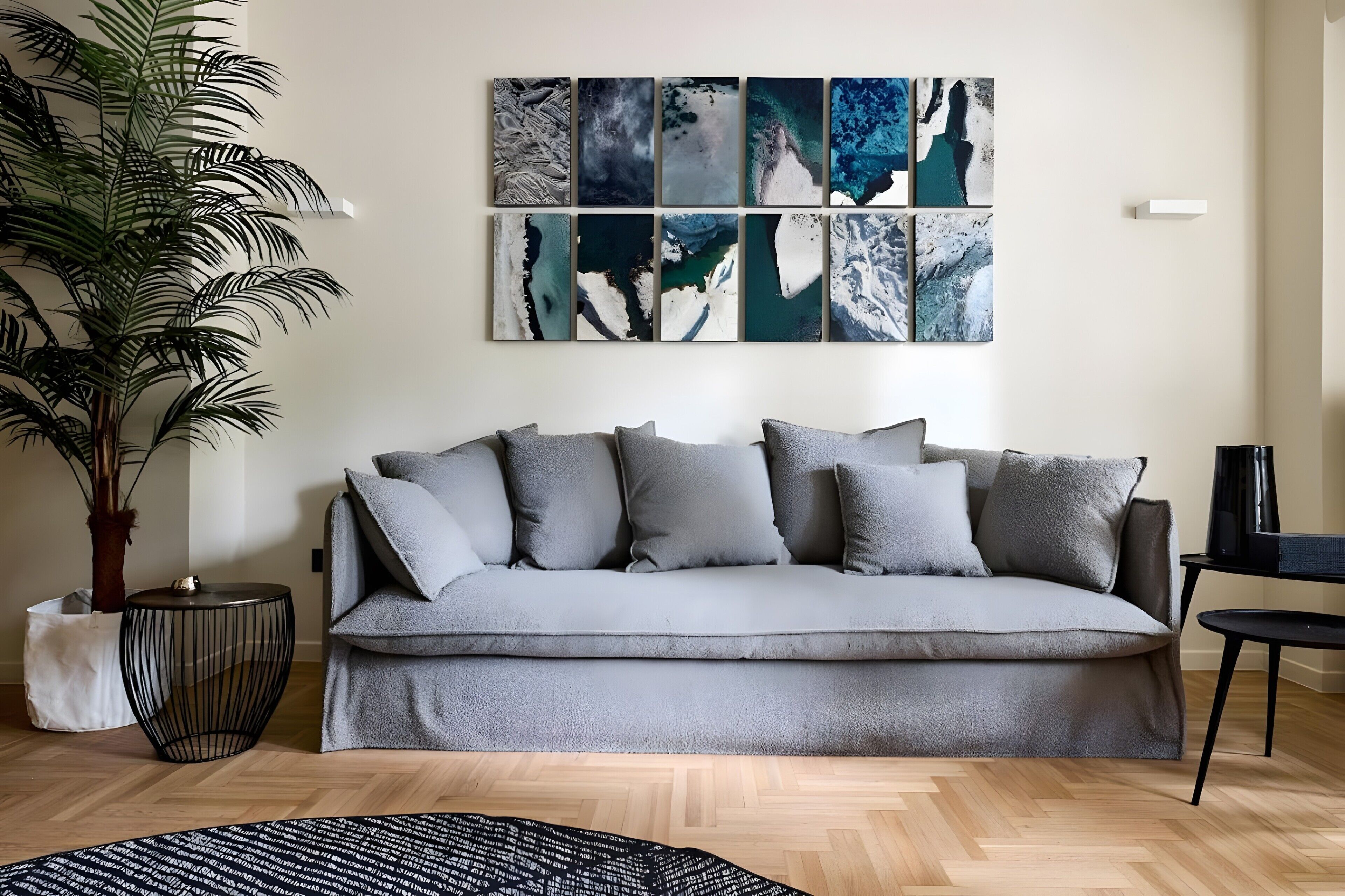 A living room with a grey sofa, a large potted plant, and a wall-mounted art piece.