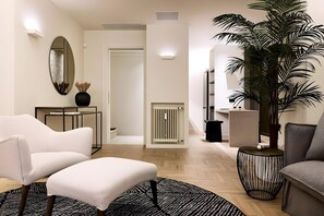 A modern living room with a white sofa, a side table, a large potted plant, and a patterned rug. - Estia Athens – Your Luxurious Urban Retreat (Athens)