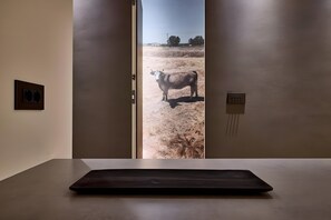 A room with a minimalist design, featuring a single table and a door leading to an outdoor area with a cow. - Estia Athens – Your Luxurious Urban Retreat (Athens)