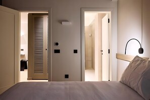 Een slaapkamer met een bed, nachtkastje, lamp en deur naar een badkamer.
