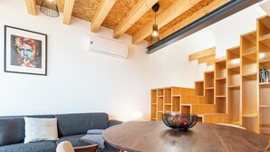 Uma sala de estar moderna com uma mesa redonda de madeira, um sofá cinza e uma estante de livros de madeira.