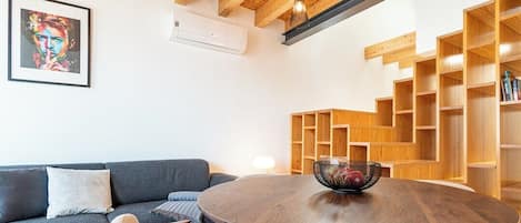 A modern living room with a round wooden table, a gray sofa, and a wooden bookshelf.