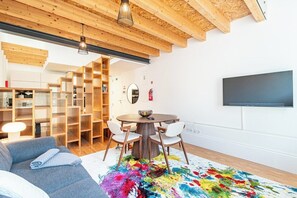 Ein modernes Wohnzimmer mit Holzbalkendecke, einem runden Esstisch und einem farbenfrohen Teppich.