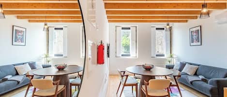 A room with a dining table and chairs, a sofa, and a fire extinguisher on the wall.