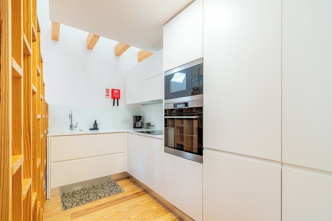 A modern kitchen with white cabinets, a built-in oven, and a coffee machine.