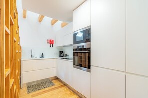 A modern kitchen with white cabinets, a built-in oven, and a coffee machine. - Modern Apt in Historic Porto's Largo da Lapa (Porto)