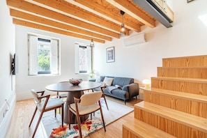 Un espai de vida modern amb una escala de fusta, una taula rodona amb seients, un sofà i una finestra gran.