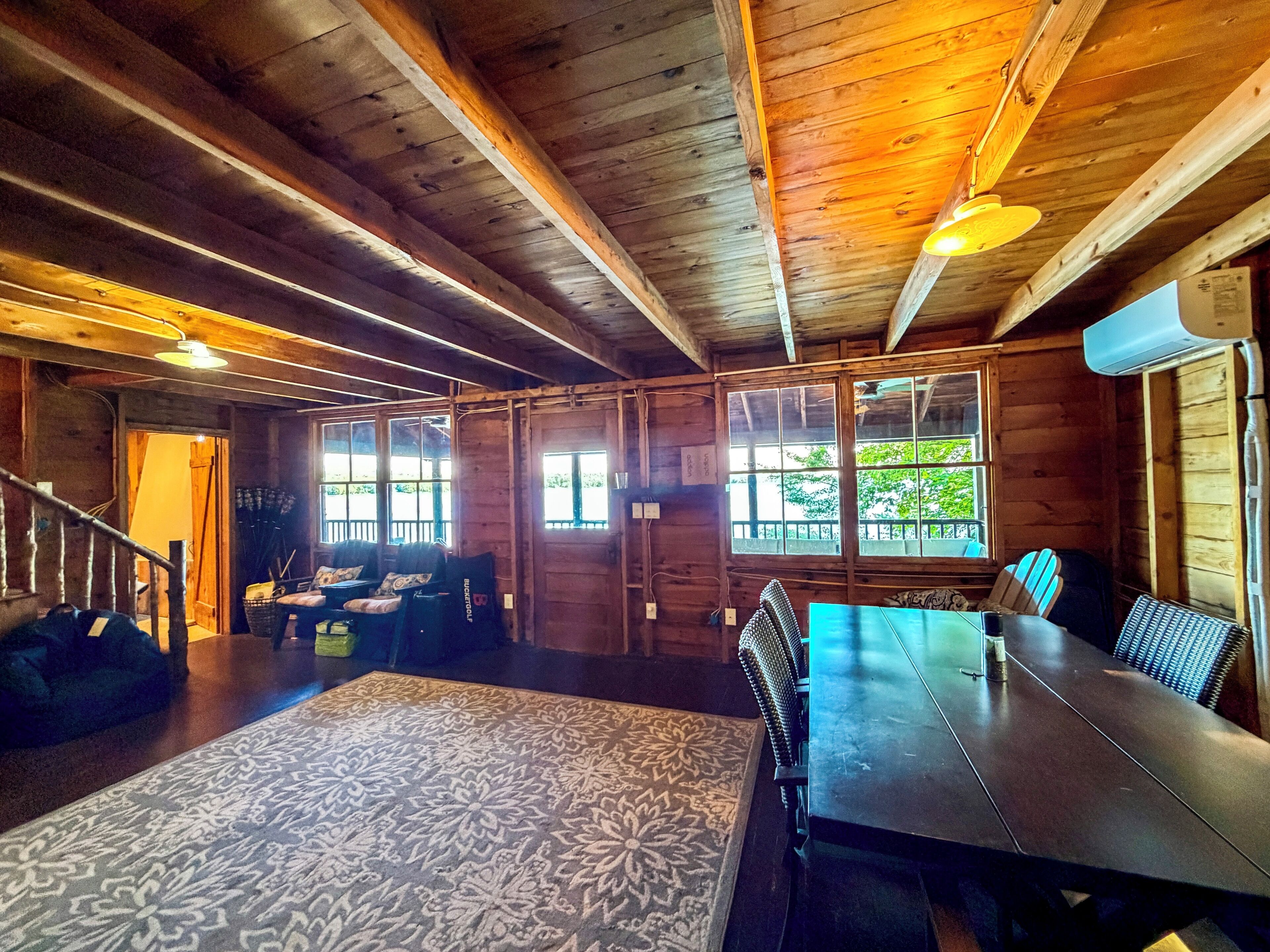 A wooden interior with a dining table, chairs, and a patterned rug.