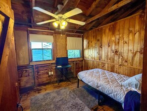 Een kamer in een chalet met een bed, een bureau, een stoel, een plafondventilator en ramen.