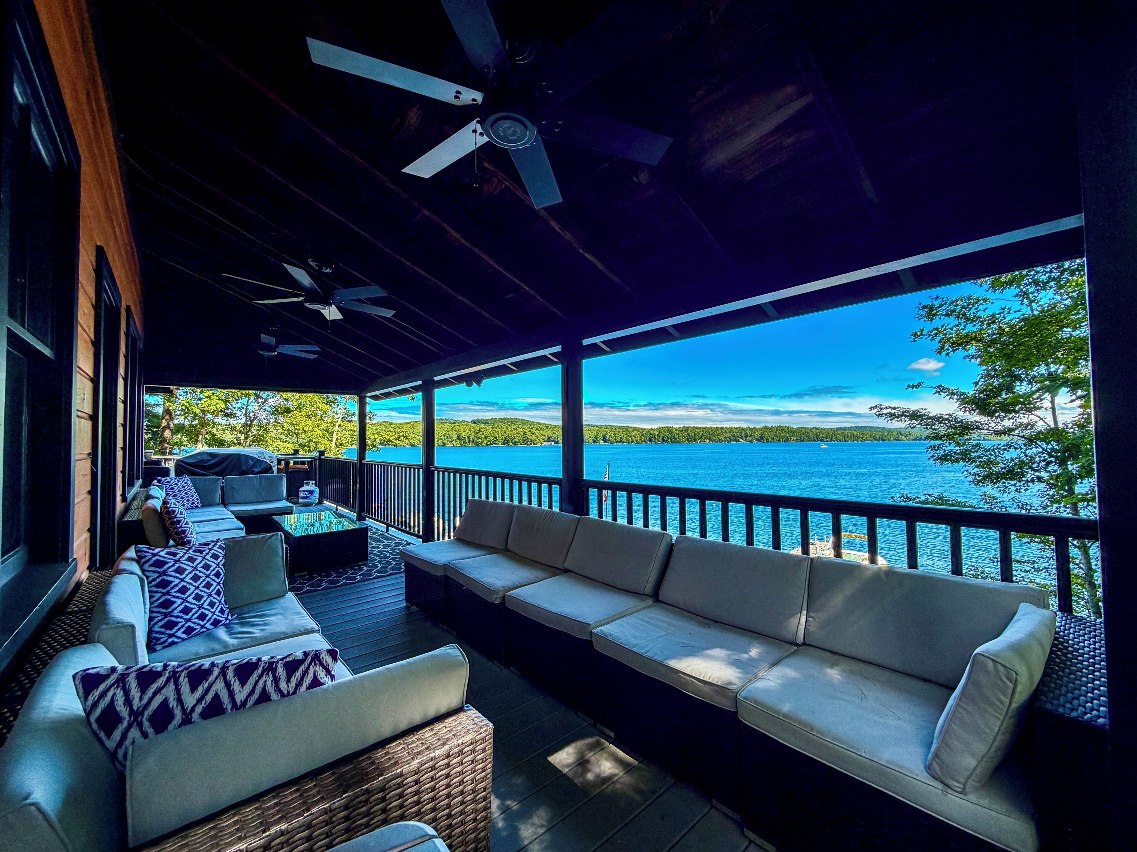 A covered outdoor seating area with a view of a lake and forest.