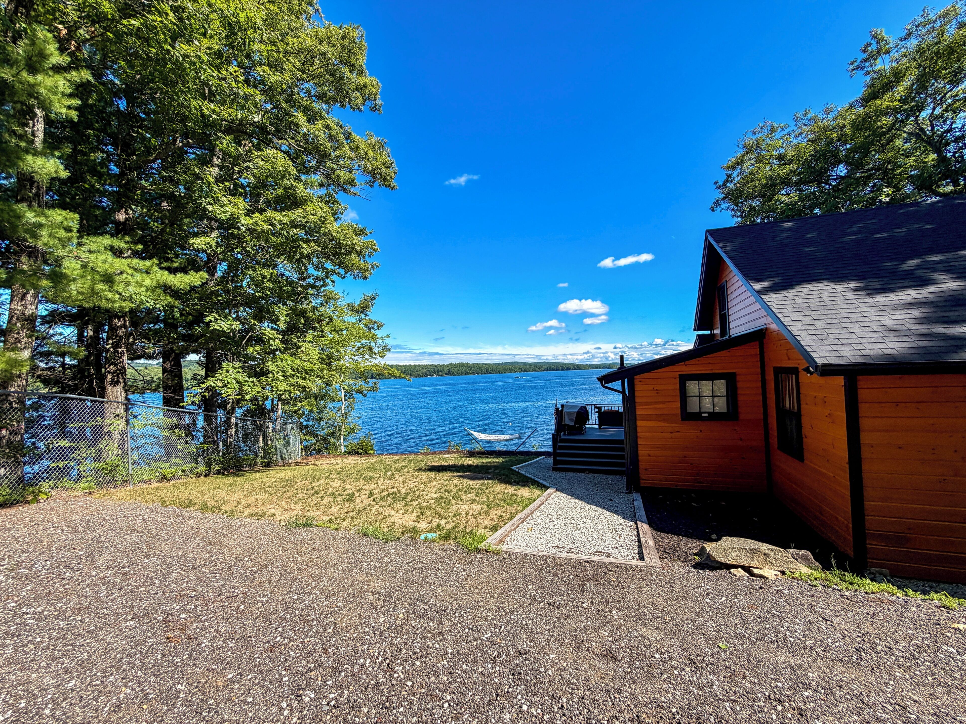Une cabane avec une allée de gravier menant à un quai, donnant sur un lac où se trouve un bateau.