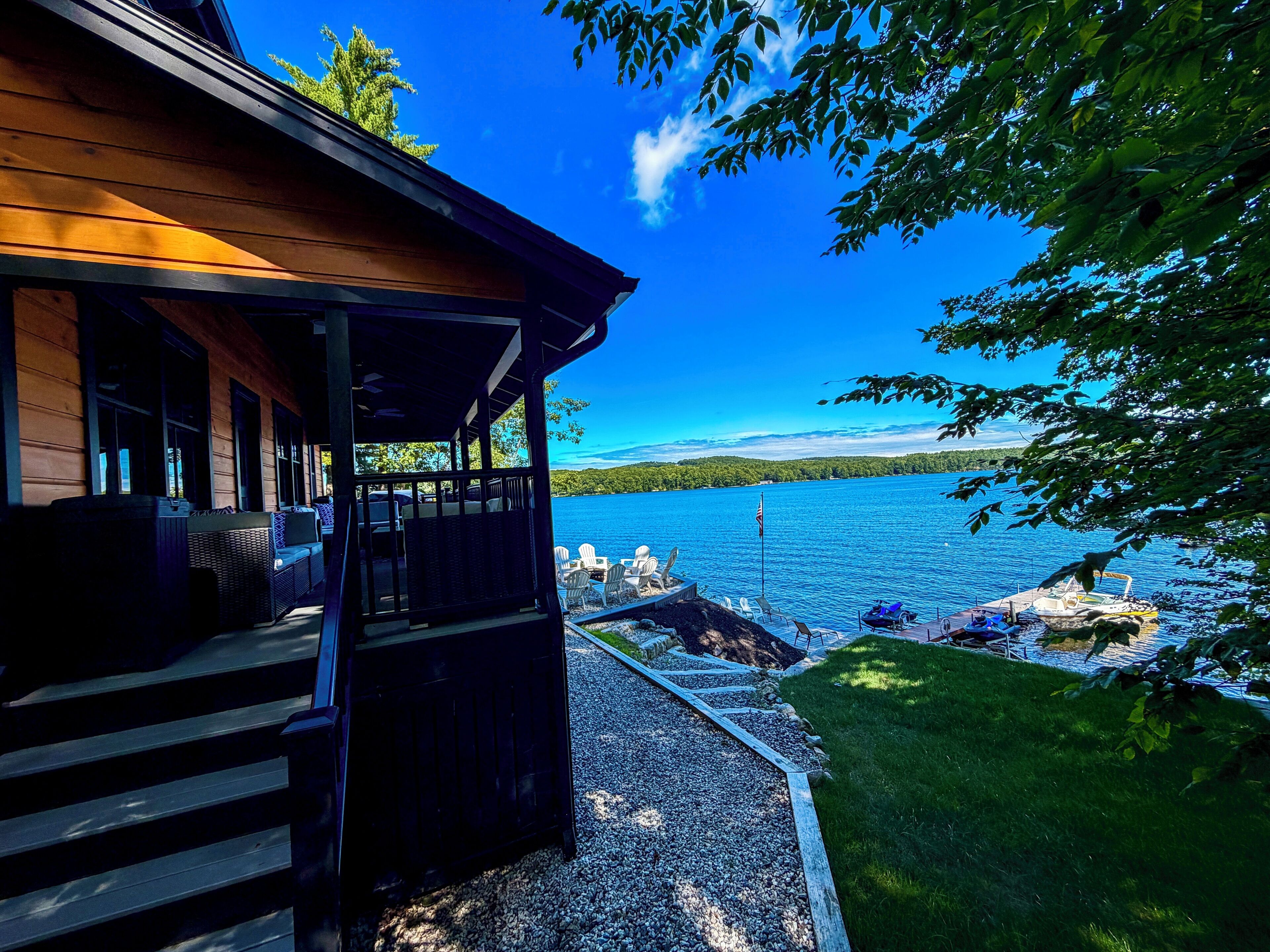 Une cabane en bois dotée d’un porche couvert, d’un chemin de gravier et offrant une vue sur un lac.