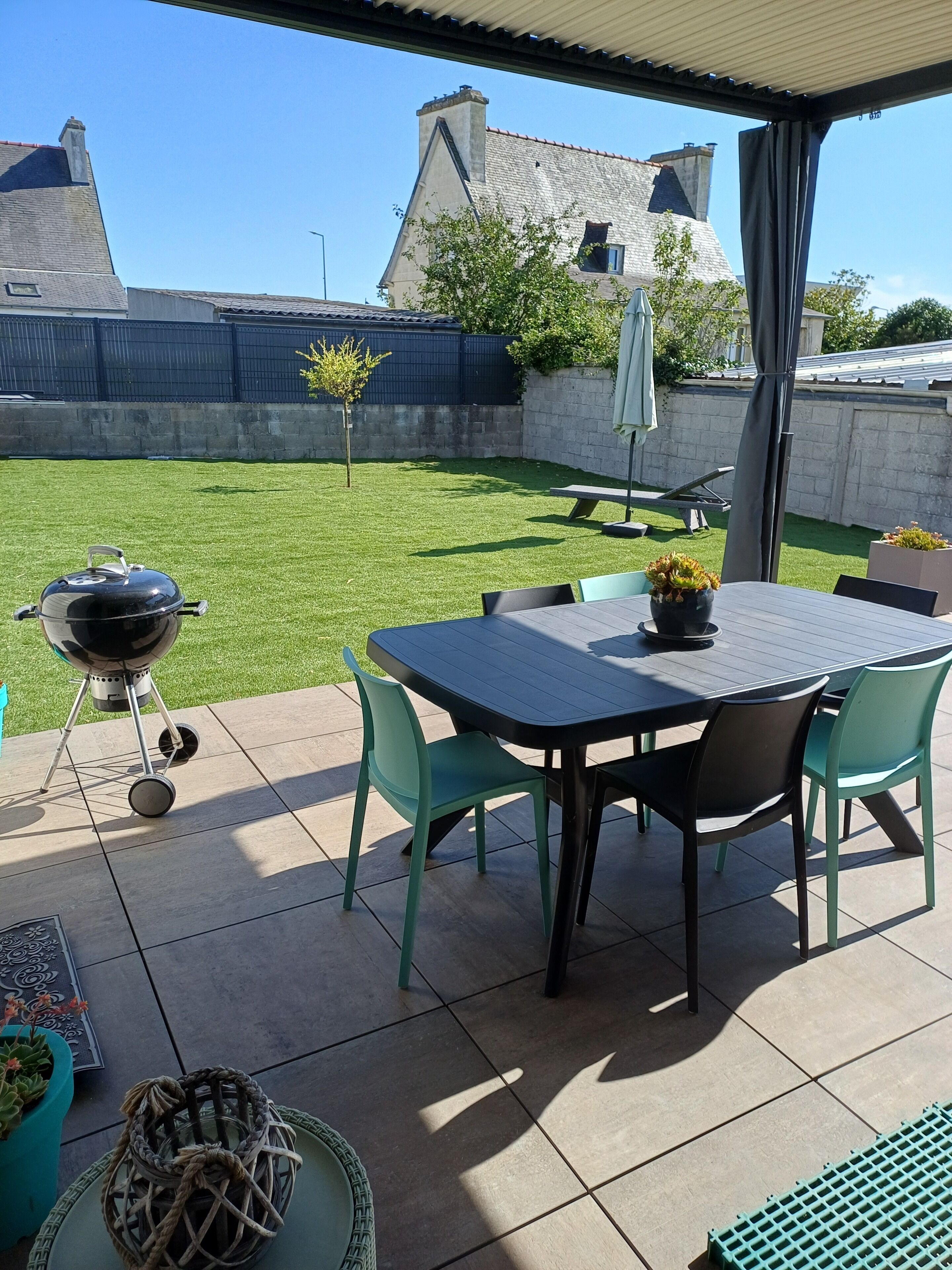 An outdoor patio with a grill, a table with chairs, and a covered area.