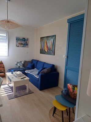 Ein Wohnzimmer mit einem blauen Sofa, einem Couchtisch, einem Bild von Segelbooten und einem Fenster mit Jalousien.