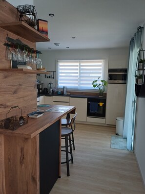 Eine moderne Küche mit Holzböden, ein Essbereich mit Barhocker und ein Fenster mit Jalousien.