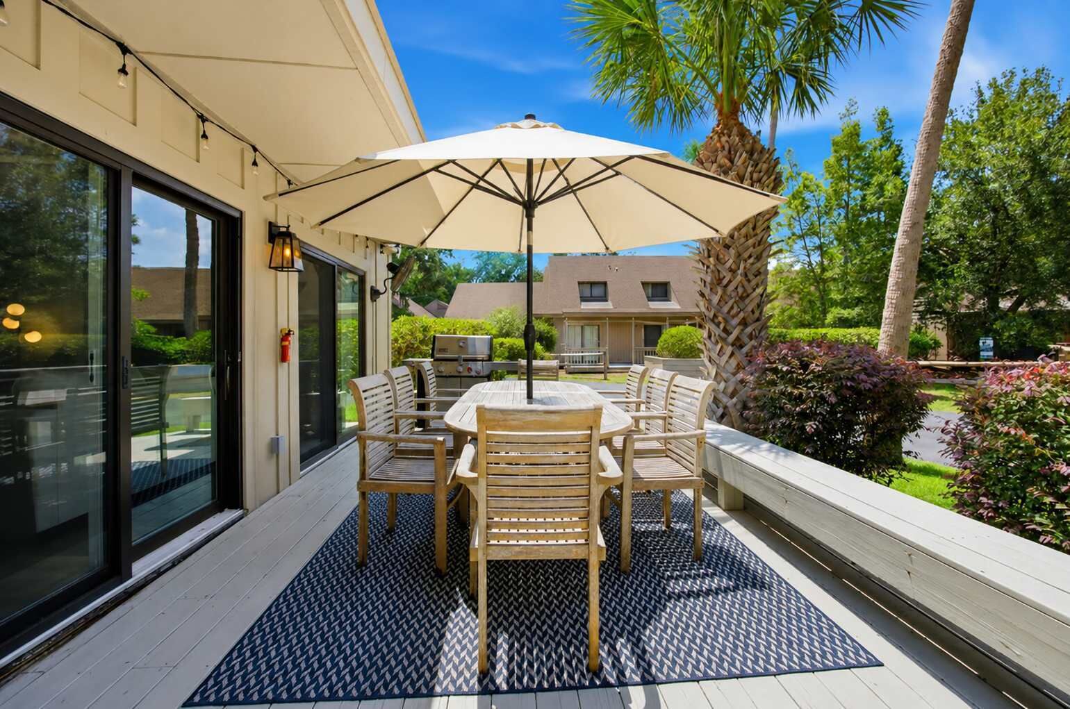 Une terrasse extérieure avec une table et des chaises, un parasol et une vue sur un bâtiment et de la verdure.