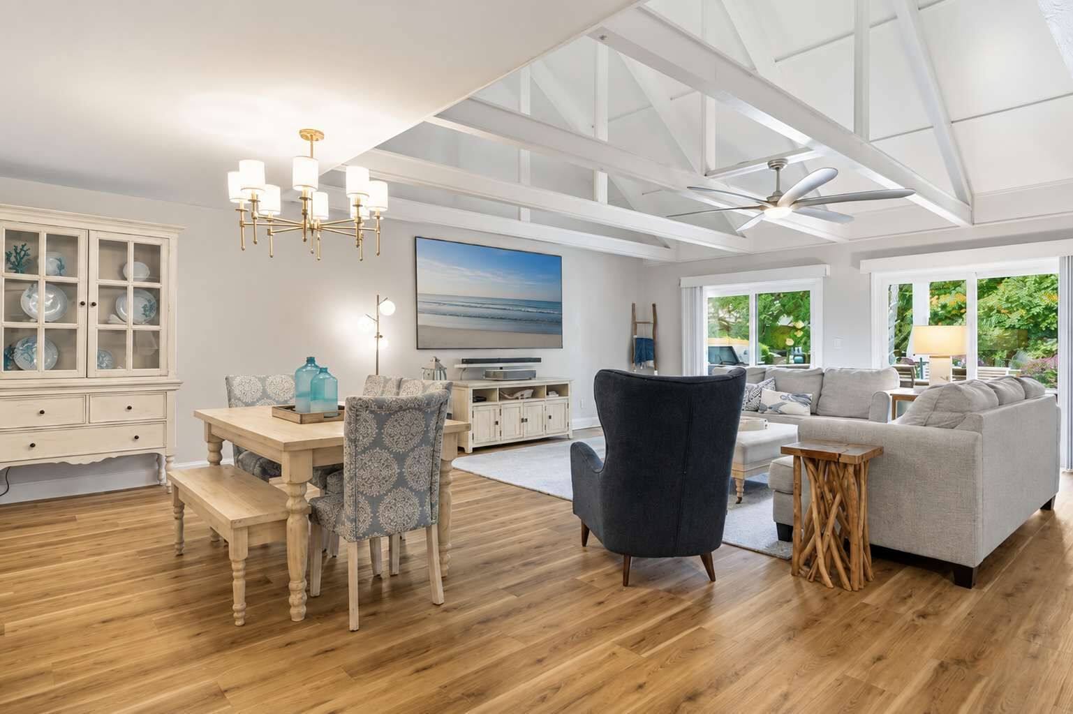 Un salon spacieux avec un plafond haut, un coin repas doté de meubles en bois et une vue sur la verdure environnante.
