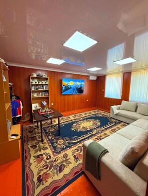 A living room with a sofa, a television mounted on the wall, a chessboard, and a bookshelf.