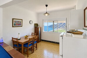 A dining area with a table and chairs, a clock, a window with a view of the ocean, and a refrigerator. - GuestReady - Villa Mountain Sea Views (Hermigua)