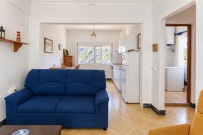 A living room with a blue sofa, a dining table, and a kitchen in the background. - GuestReady - Villa Mountain Sea Views (Hermigua)
