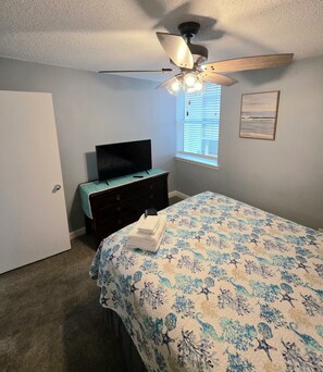A bedroom with a bed, a dresser, a television, a ceiling fan, and a window with blinds. - Wonderful 3-bedroom condo with ocean views in charming Gulf Shores (Gulf Shores)