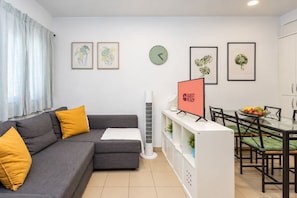 A modern living room with a grey sofa, yellow cushions, a dining area with a glass table and chairs, and a 'GUEST READY' sign. - GuestReady - Town Centre Apartment (Tazacorte)
