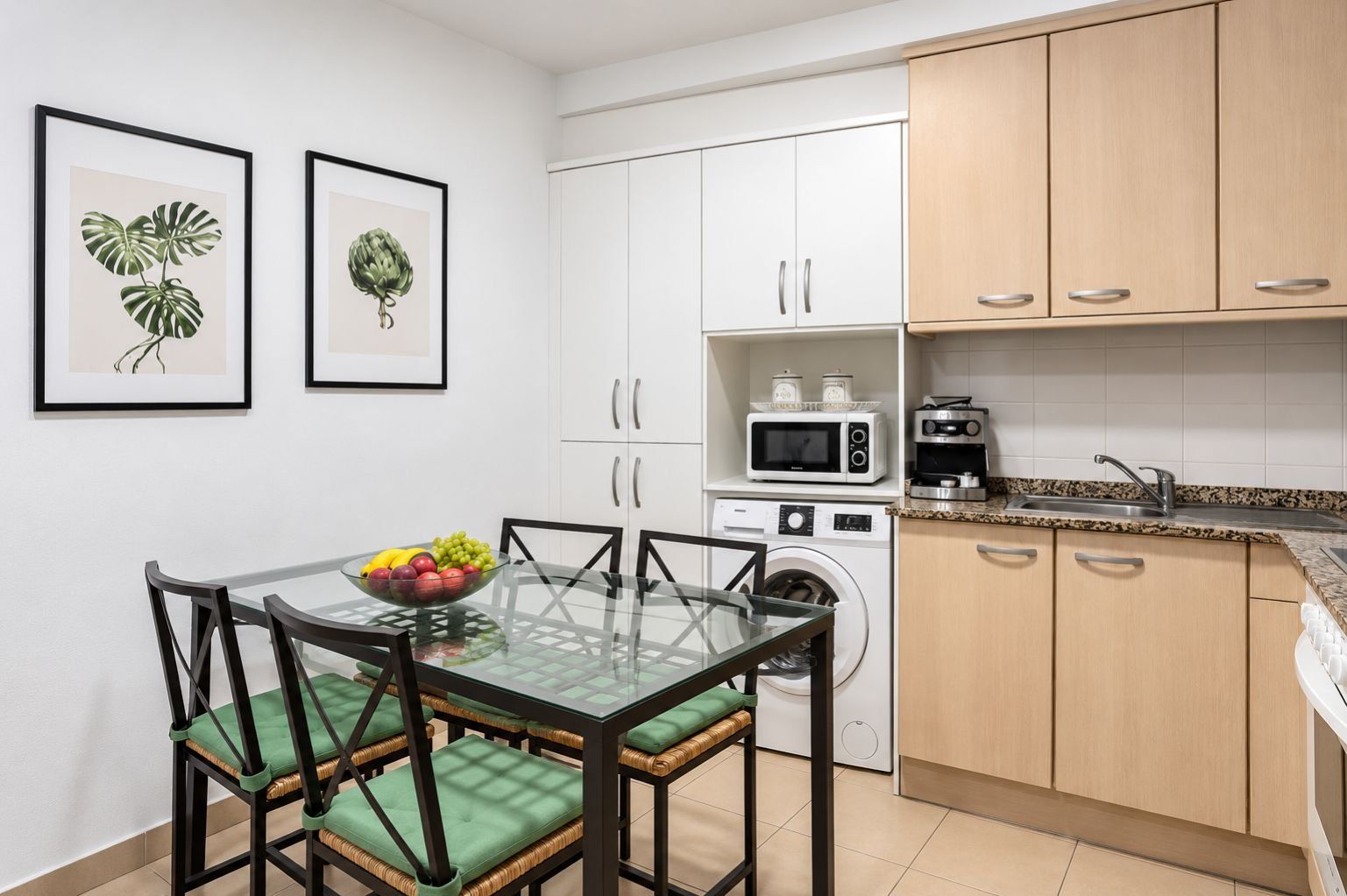 Cozinha compacta com armários brancos, uma mesa de jantar com tampo de vidro e uma máquina de lavar.