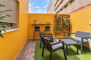 A small outdoor patio with a table and chairs, a wooden planter with plants, and a window with blinds. - GuestReady - Town Centre Apartment (Tazacorte)