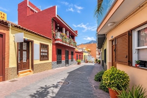 A narrow cobblestone street lined with colorful buildings, some with balconies and potted plants. - GuestReady - Town Centre Apartment (Tazacorte)