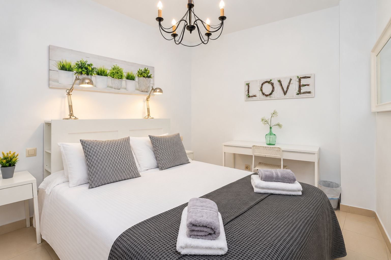 Un dormitorio moderno con una cama grande, lámparas de noche, un escritorio y una estantería con plantas en la pared.