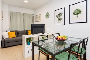 A modern living room with a sofa, a flat-screen TV, a glass dining table with chairs, and artwork on the walls. - GuestReady - Town Centre Apartment (Tazacorte)
