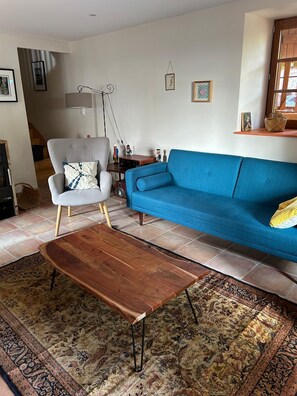 Ein Wohnzimmer mit einem blauen Sofa, einem grauen Sessel, einem Holztisch und einem Teppich mit Muster.