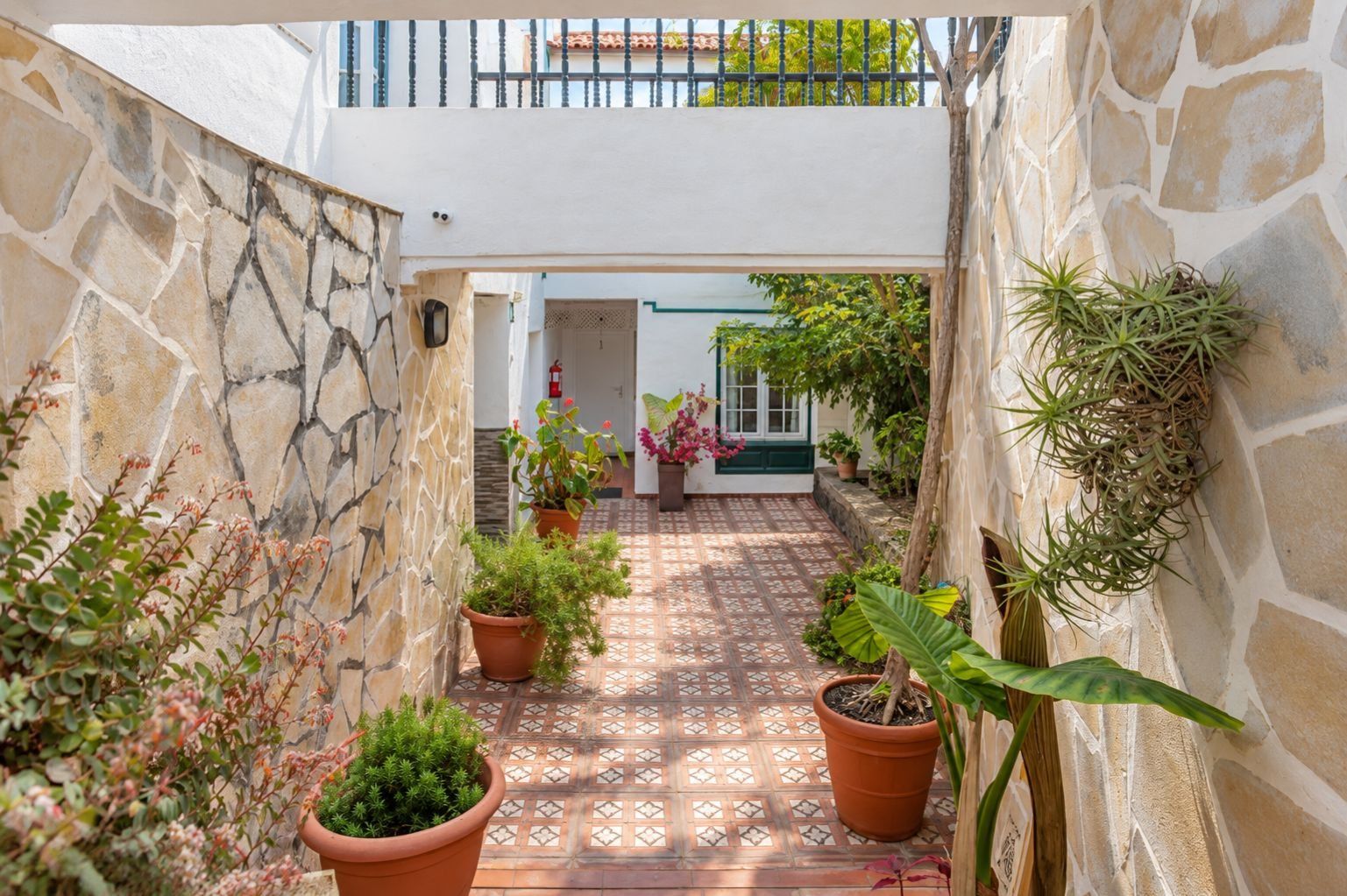 Un patio estrecho con paredes de piedra, plantas en macetas y suelo de baldosas.