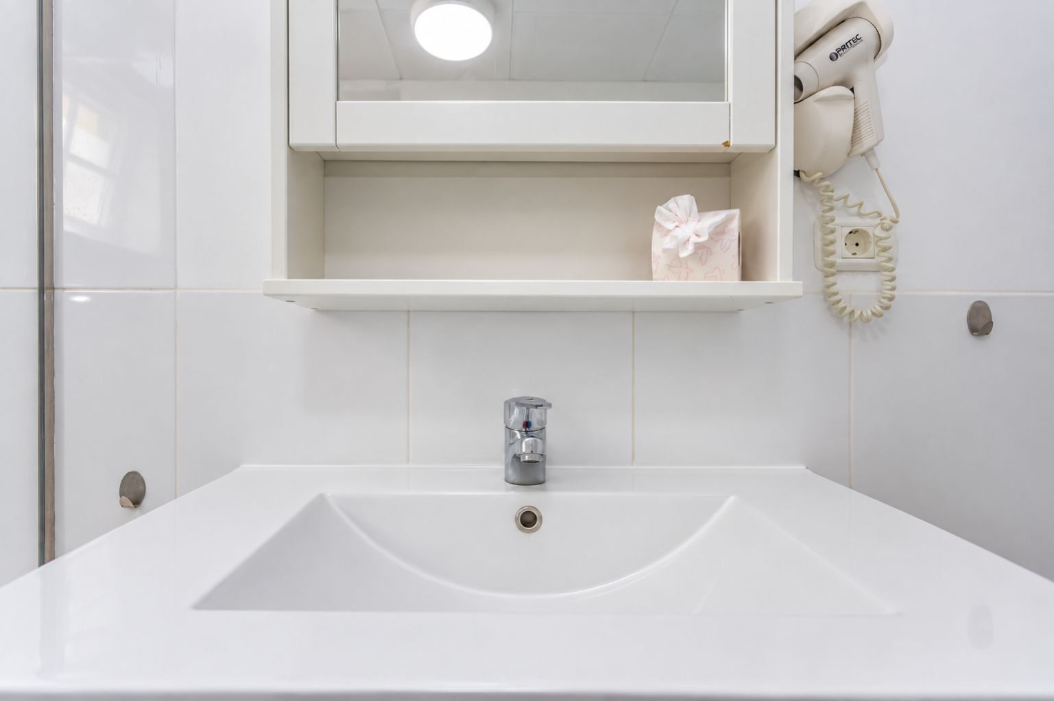 A bathroom with a white sink, a mirror above it, and a hairdryer on the wall.